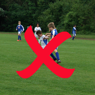 Das Symbolbild zeigt junge Fußballer*innen beim Fußballspiel auf einem Rasenplatz in Frechen - hier im Sportpark Herbertskaul. Im Bild ist ein rotes "X" erkennbar, dieses symbolisiert, dass der Platz gesperrt ist.