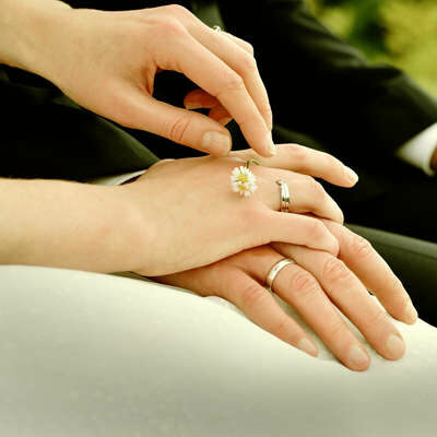 Das Foto zeigt die Hände von Brautleuten. Beide tragen an ihrer rechten Hand einen Ehering.