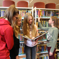 Das Bild zeigt vier Mädchen, die sich Bücher am Regal anschauen