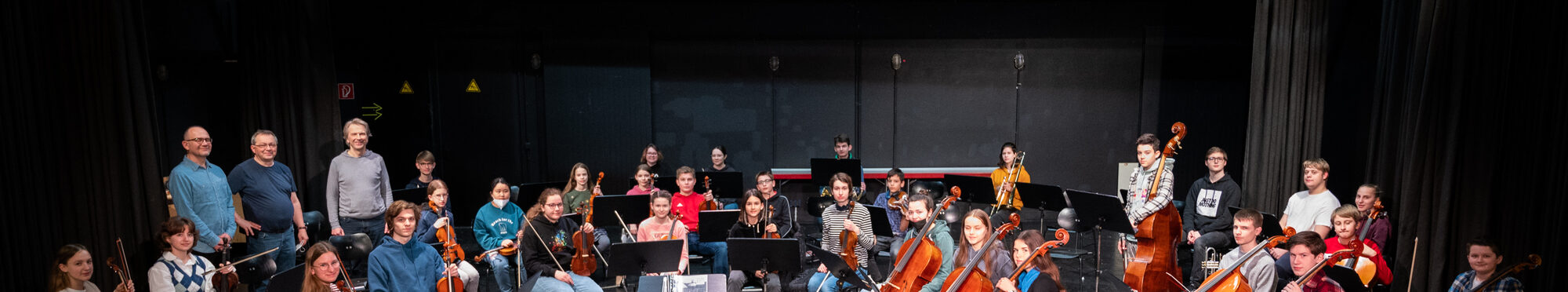 Die Mitglieder der Rhein-Erft-Philharmonie sitzen und stehen mit ihren Instrumenten auf einer Bühne.
