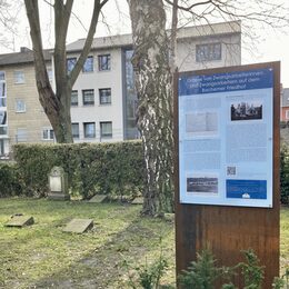 Infotafel mit Text und Bildern zu Gräbern von Zwangsarbeiterinnen und Zwangsarbeitern auf dem Bachemer Friedhof