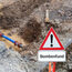 Das Foto zeigt eine Baugrube die mit einem Hinweisschild auf einen Bombenfund gesichert ist.