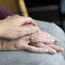 Das Bild zeigt wie eine Hand die Hände von einer Seniorin berührt.